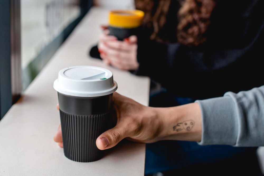 Man in cafe gripping the Circular Returnable Cup which is rested on counter top.
