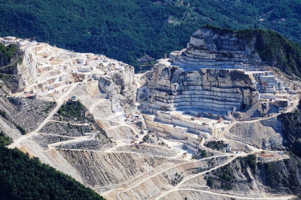 Large open quarry in tree-covered mountainous region.